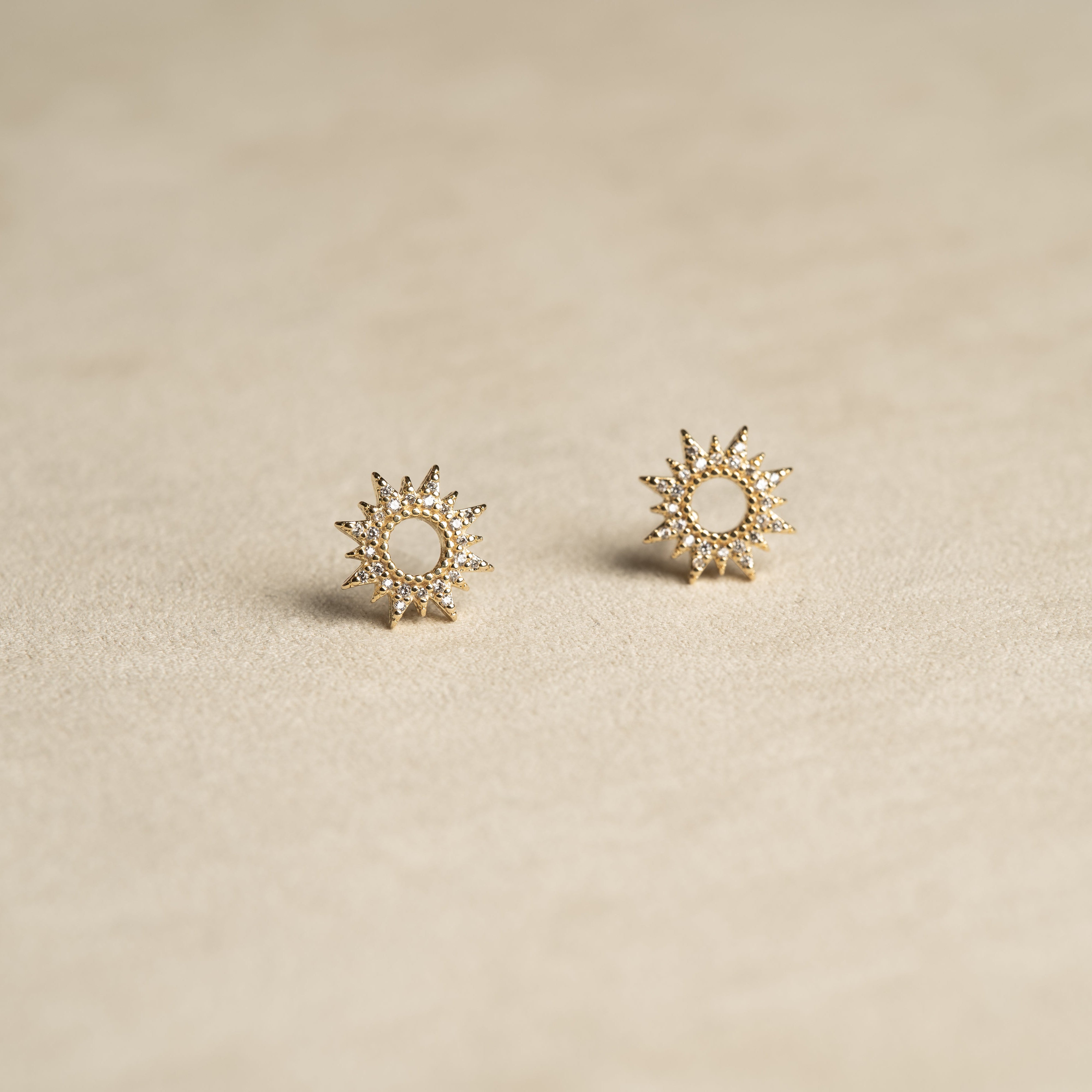 Pair of gold sun-shaped earrings on a beige background
