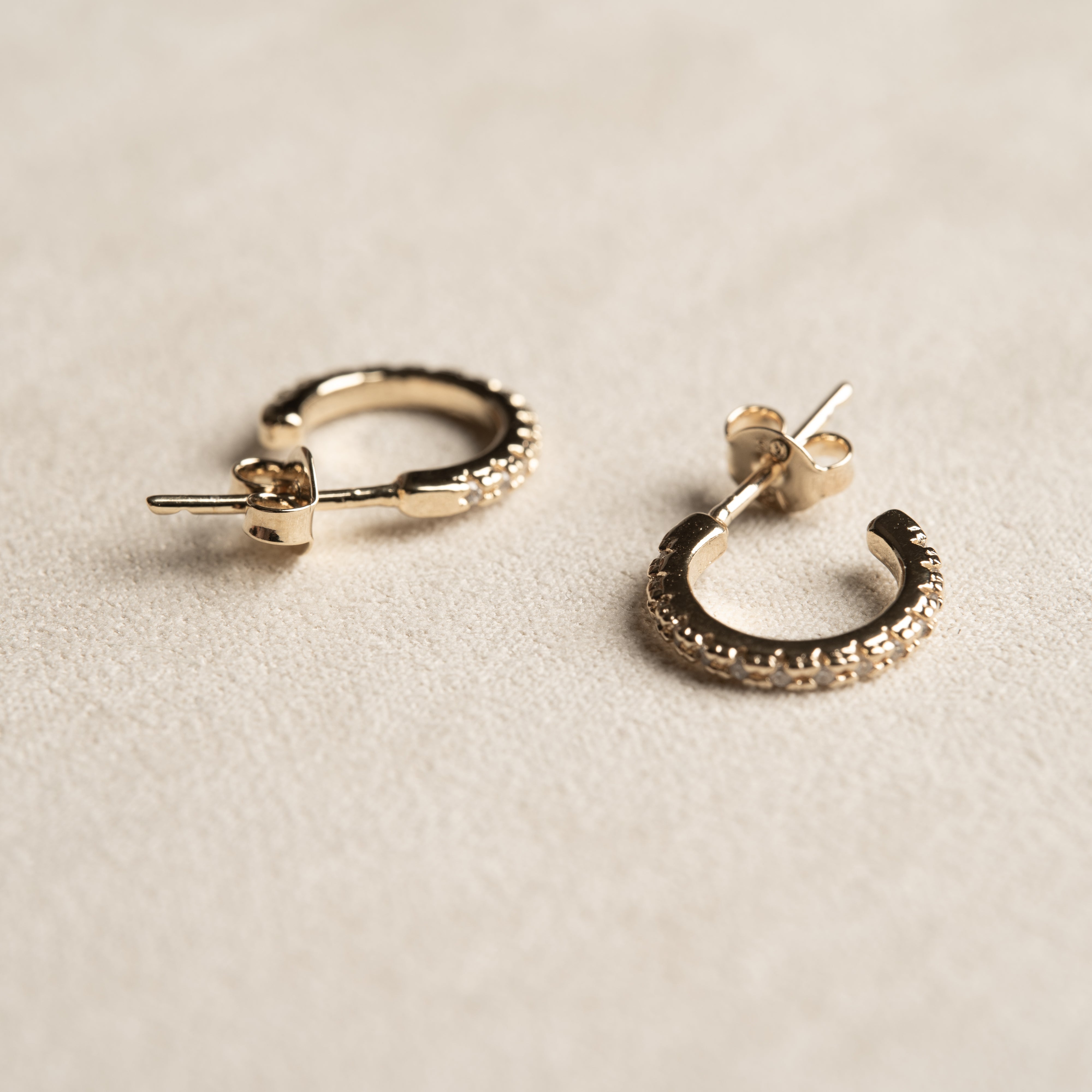 Minimalist gold semi hoop earrings with tiny crystals inlaid on a beige background