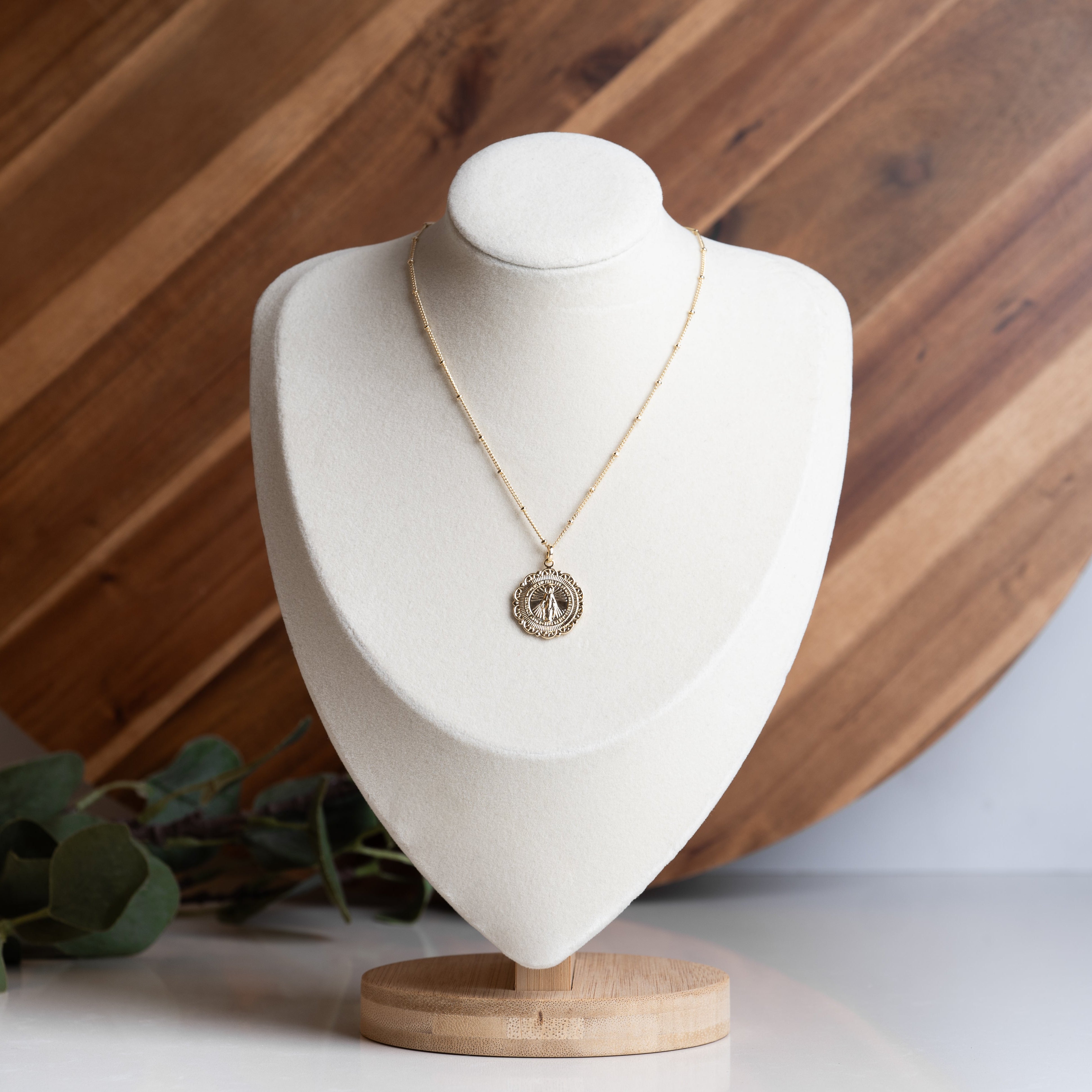 Miraculous Medal Necklace on a white holder with a wooden background